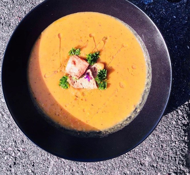 En gul soppa i en svart skål med små krutonger, lite olja och persilja i en kreativ framduktning