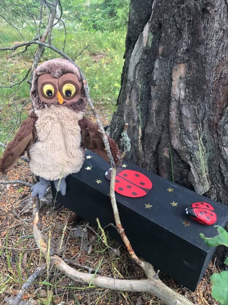 Öppen förskola har en nalle-uggla som sitter på en bänk med tränyckelpigor på vid ett stort träd