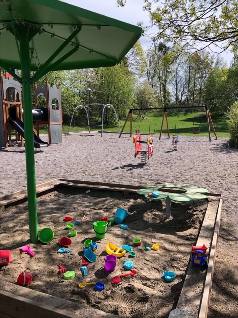 Öppna förskolan lek på gården med sandlåda, gungor och rutchkana, sandlåda och gräsmatta och natur