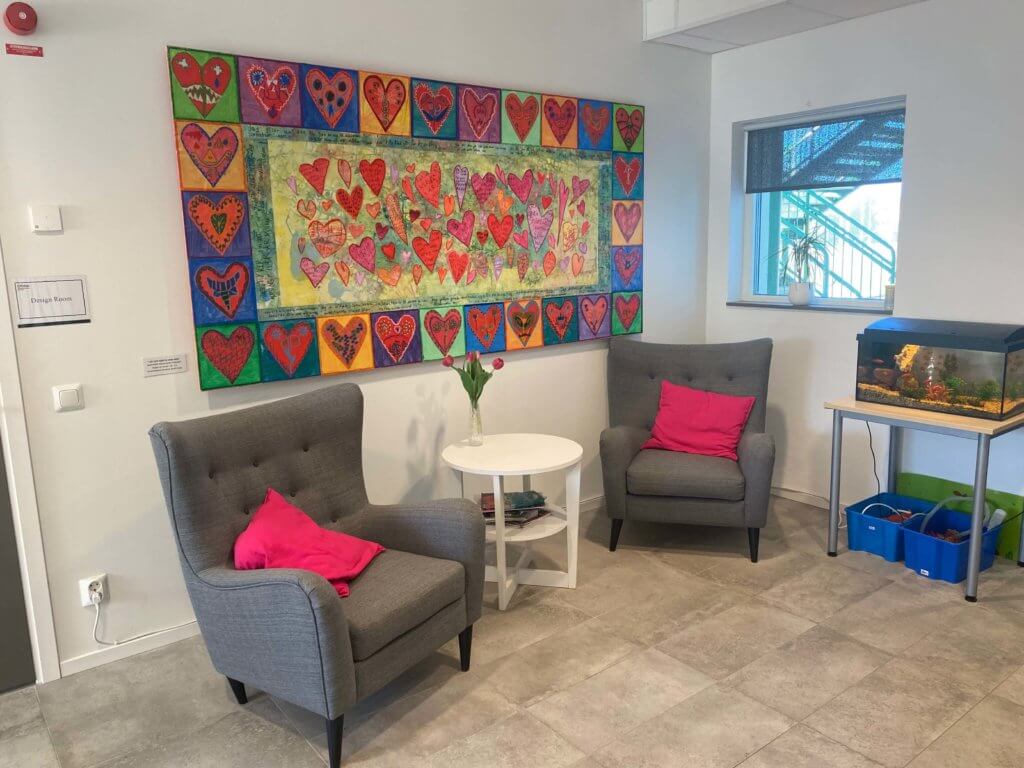 Mysig hörna med två fåtöljer och en stor tygbild som hänger bakom med hjärtan på